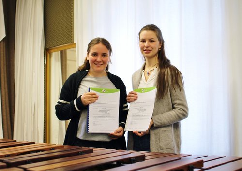 Zwei Schülerinnen der BFS Musik stehen hinter einem Marimbaphon und halten ihre Kompositionen in den Händen.