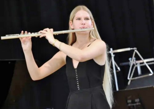 Schülerin Chiara Filzek steht auf einer Bühne vor schwarzem Hintergrund und spielt Querflöte.