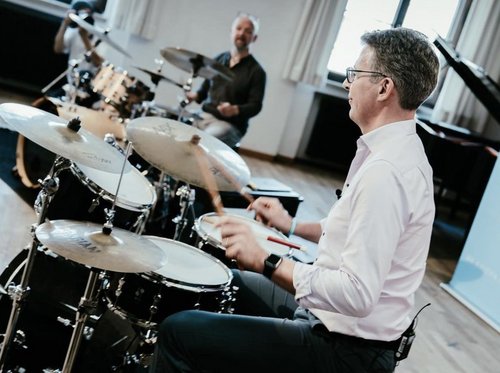 Markus Blume sitzt an einem Drumset und hält Sticks in den Händen.